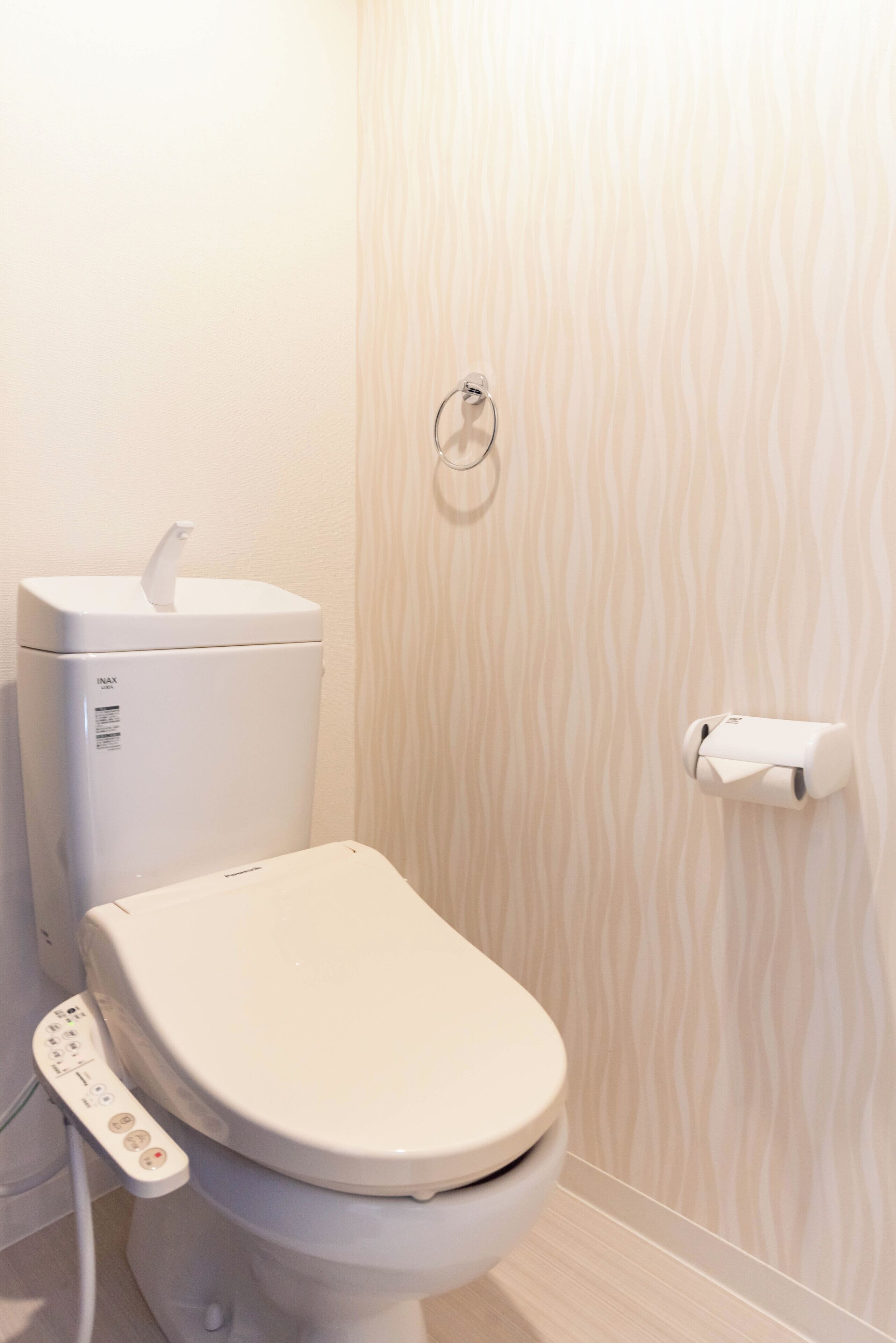 Uma casa de banho moderna com um painel de controlo, um suporte para papel higiénico e uma parede com padrão.