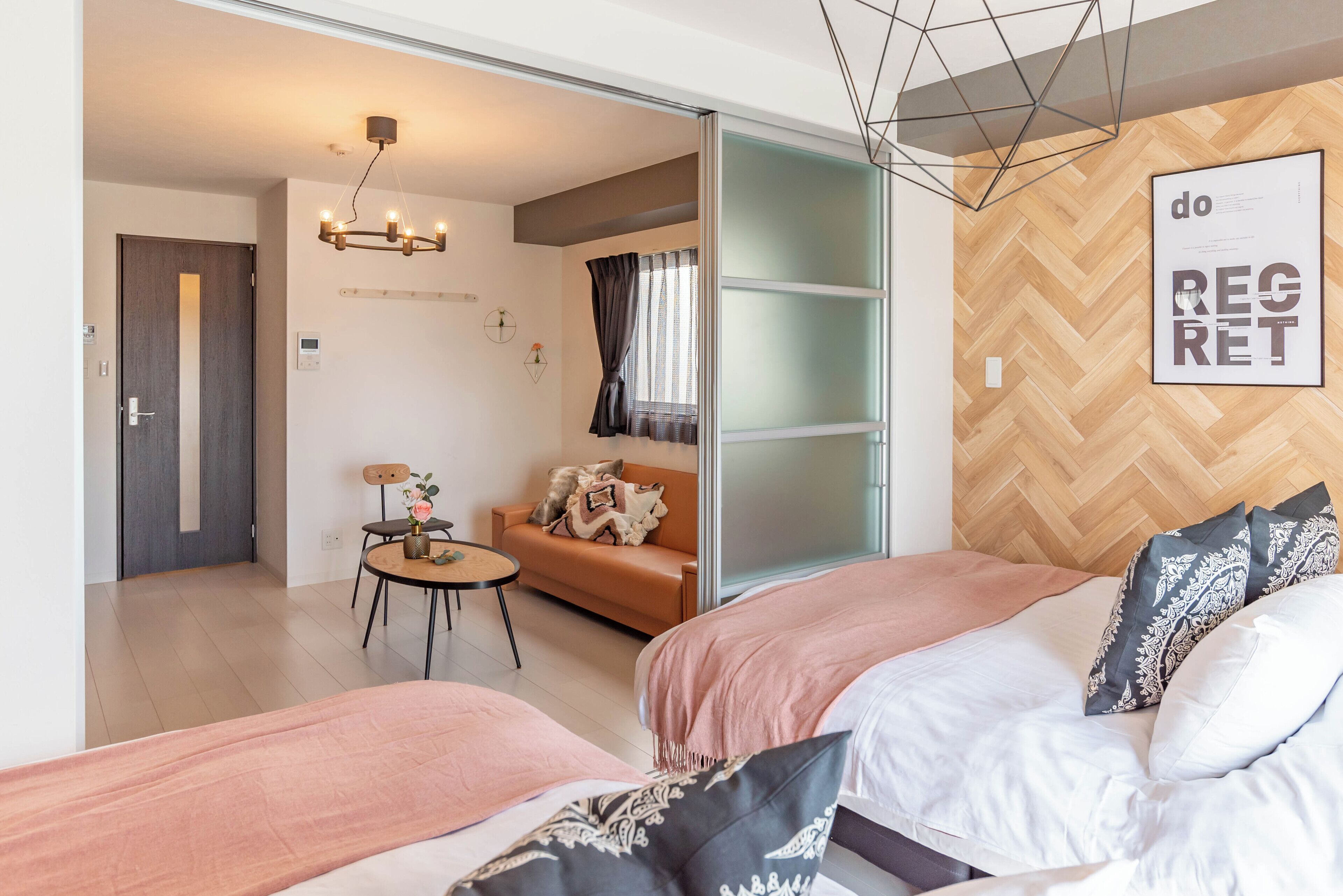 A modern hotel room with a bed, a sofa, a small table with a vase, and a wall-mounted artwork.