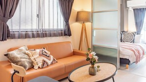 A modern hotel room with a sofa, a small round table, a floor lamp, and a bed with a large mirror. - Bijou Suites Bloom (Osaka)