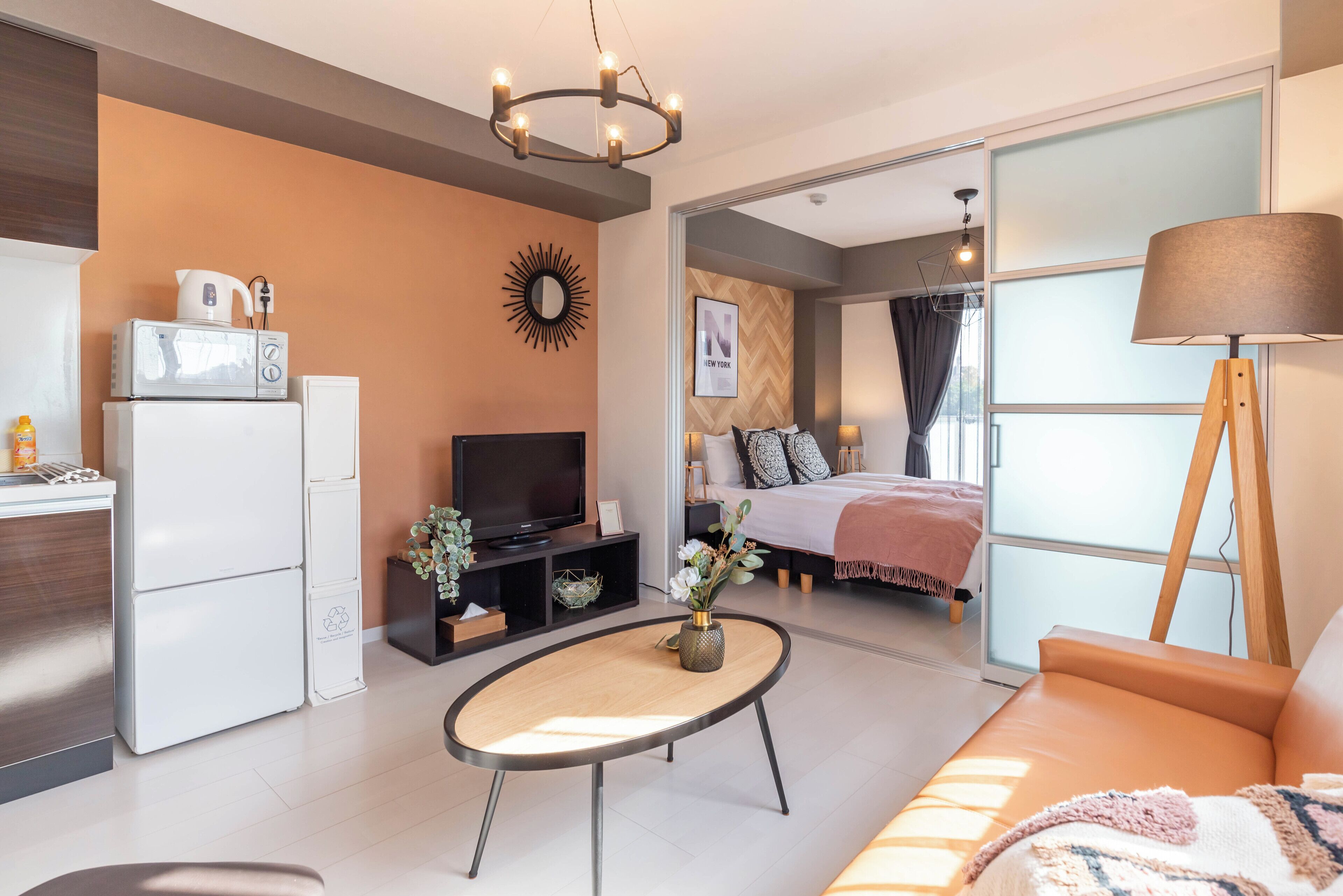 A modern living room with a sofa, a coffee table, a TV, and a kitchen area with a fridge and microwave.