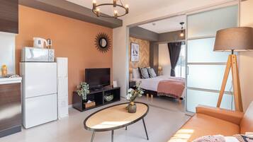 A modern living room with a sofa, a coffee table, a TV, and a kitchen area with a fridge and microwave.