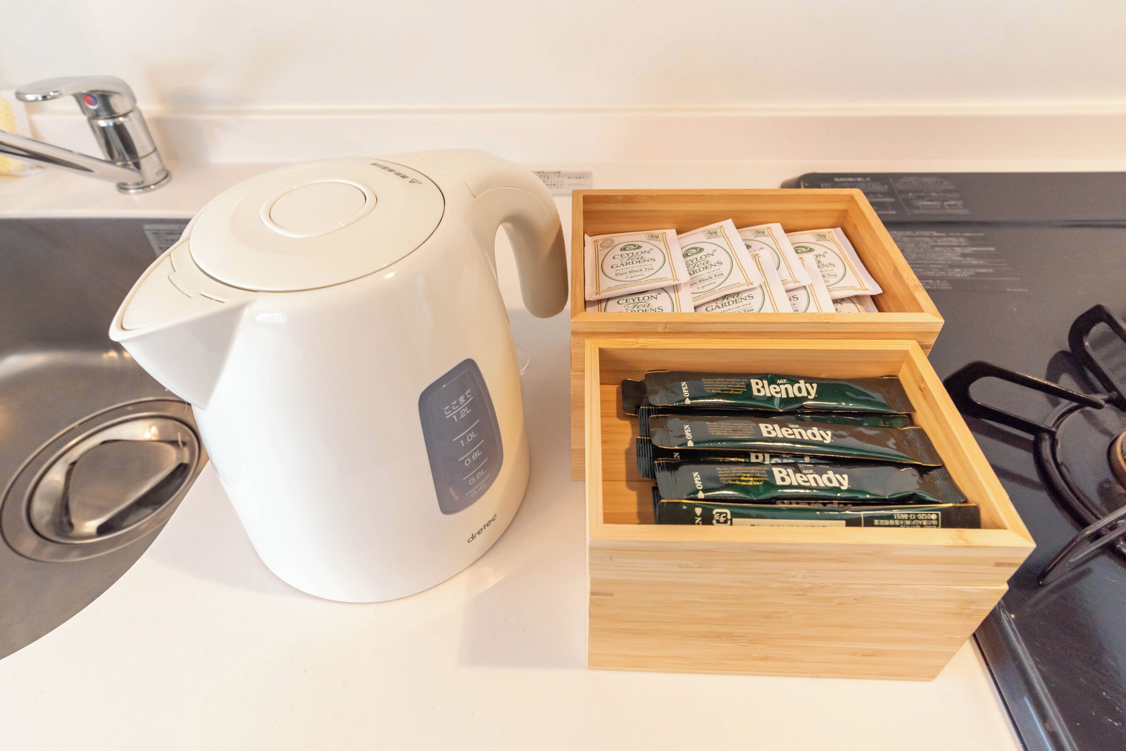 A kitchen with a white kettle and a wooden box containing packets labeled 'Blendy'.
