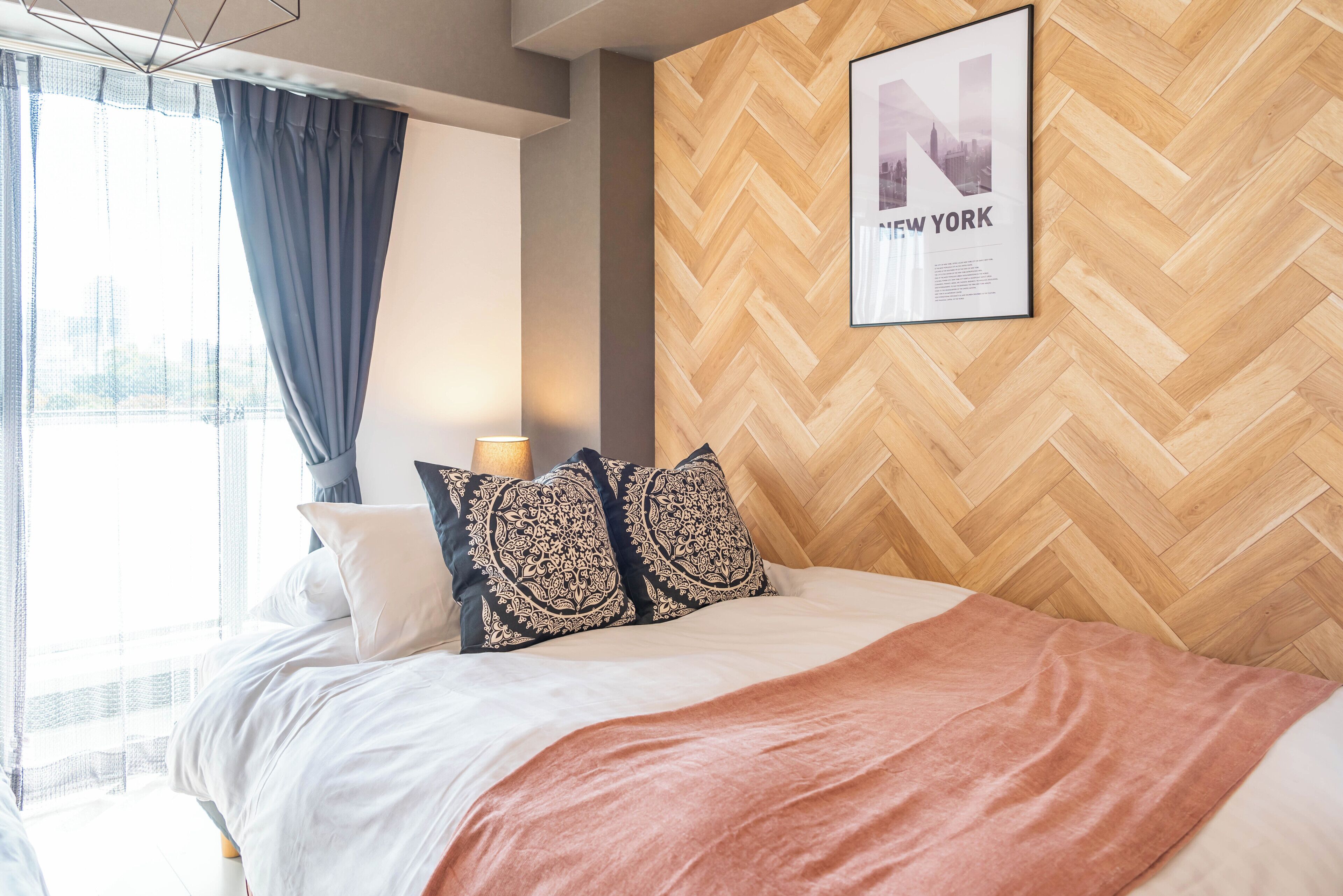 Un moderno cuarto de hotel con una cama, almohadas estampadas, un cuadro en la pared y vistas de la ciudad a través de la ventana.