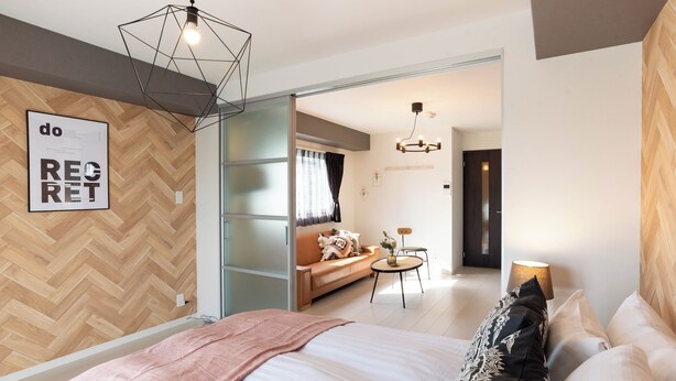 A modern bedroom with a large bed, a herringbone-patterned wall, and a geometric light fixture. - Bijou Suites Bloom (Osaka)
