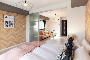 A modern bedroom with a large bed, a herringbone-patterned wall, and a geometric light fixture. - Bijou Suites Bloom (Osaka)