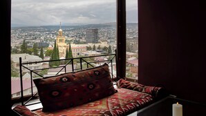 A room with a view of a cityscape, a cushioned seat with a patterned cushion, and a lit candle on a table. - Andza Tbilisi Hotel (Tbilisi)