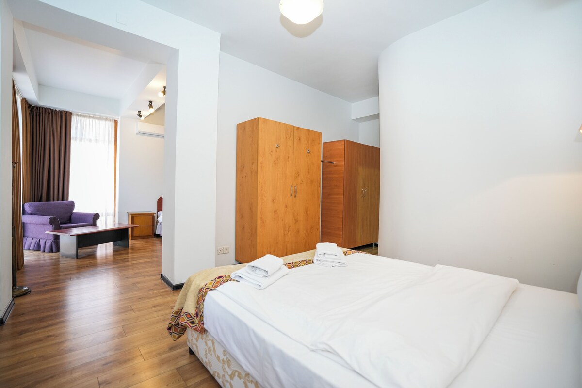 Habitació d'hotel amb un llit gran, un armari de fusta i una zona de seients amb un sofà i una taula.