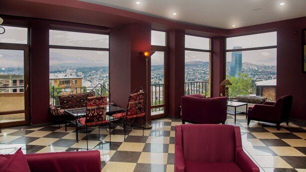 A spacious room with large windows offering a city view, checkered flooring, and red upholstered furniture. - Andza Tbilisi Hotel (Tbilisi)