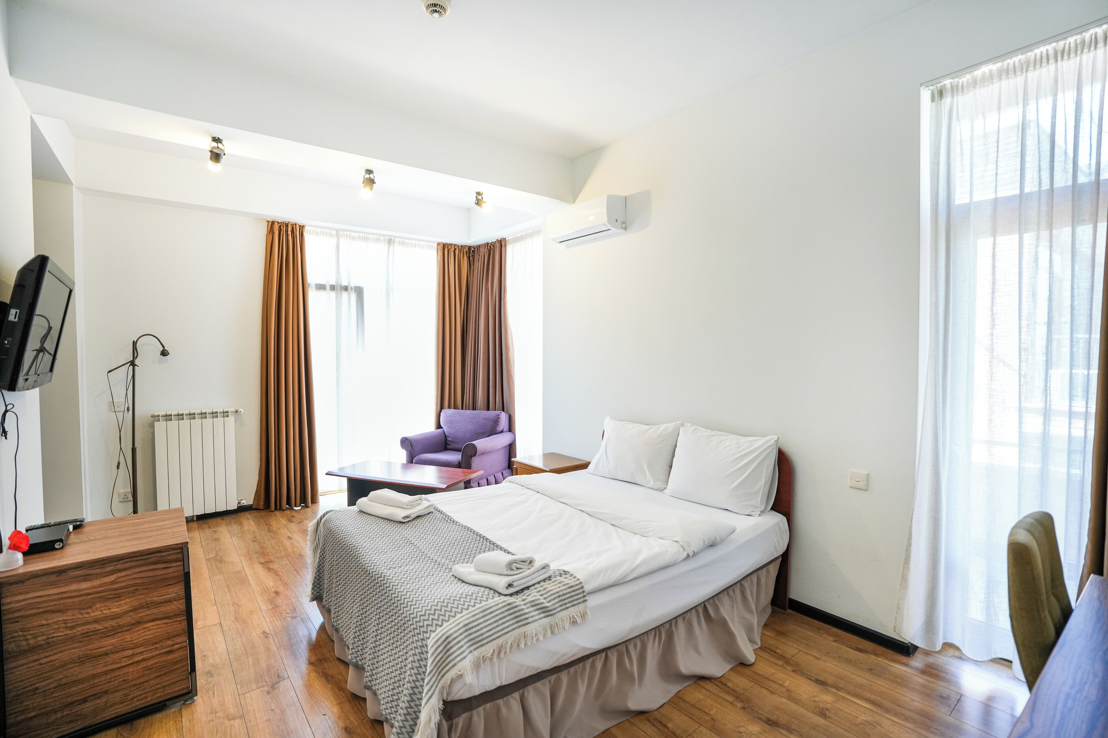 A modern hotel room with a large bed, a desk, a chair, and a view of the city through the window.