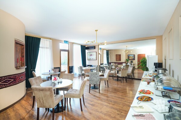 A hotel dining area with round tables, chairs, and a buffet line with various food items. - Andza Tbilisi Hotel (Tbilisi)