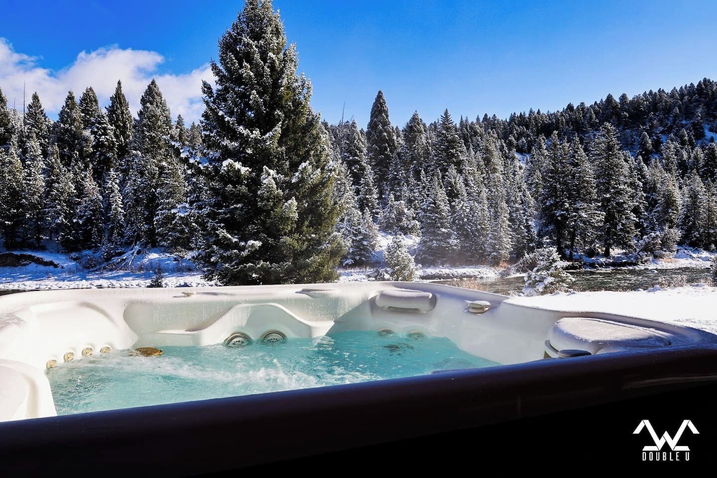 A hot tub in a snowy forest with a clear blue sky.