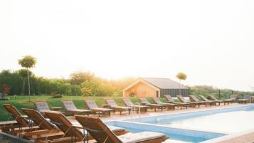 Un espace aménagé au bord de la piscine, avec des chaises longues en bois et un petit bâtiment en arrière-plan.