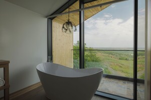 A modern bathroom with a freestanding bathtub, large windows, and a view of a green landscape.