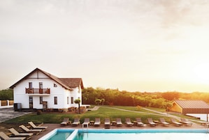 A large white building with a balcony, a swimming pool with lounge chairs, and a well-maintained lawn.