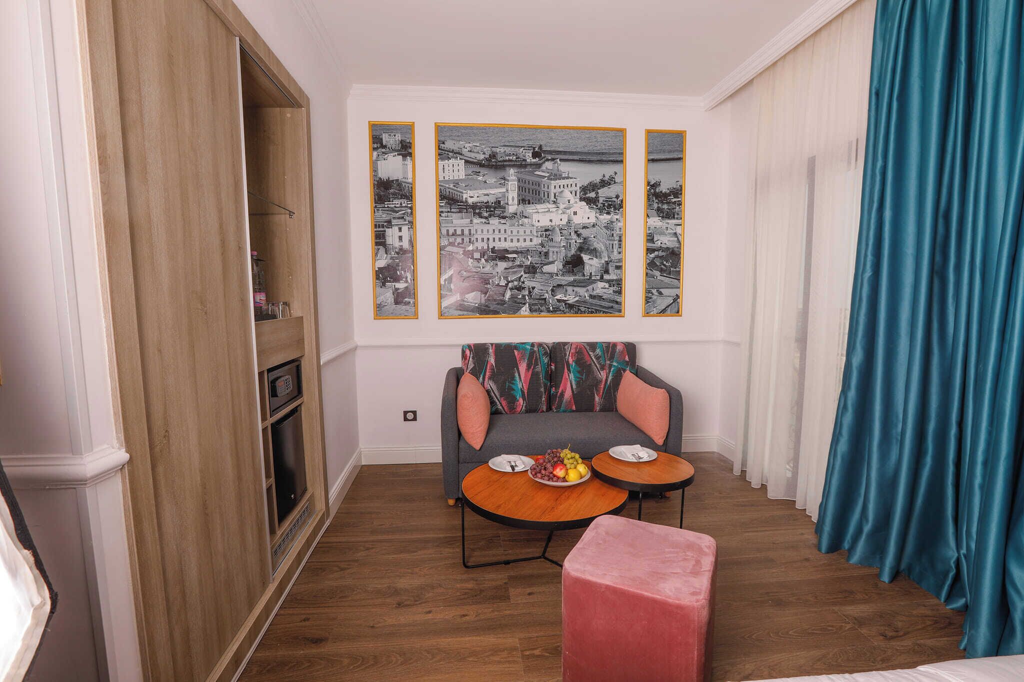 A small room with a sofa, two round tables, a red ottoman, and three black-and-white photographs on the wall.