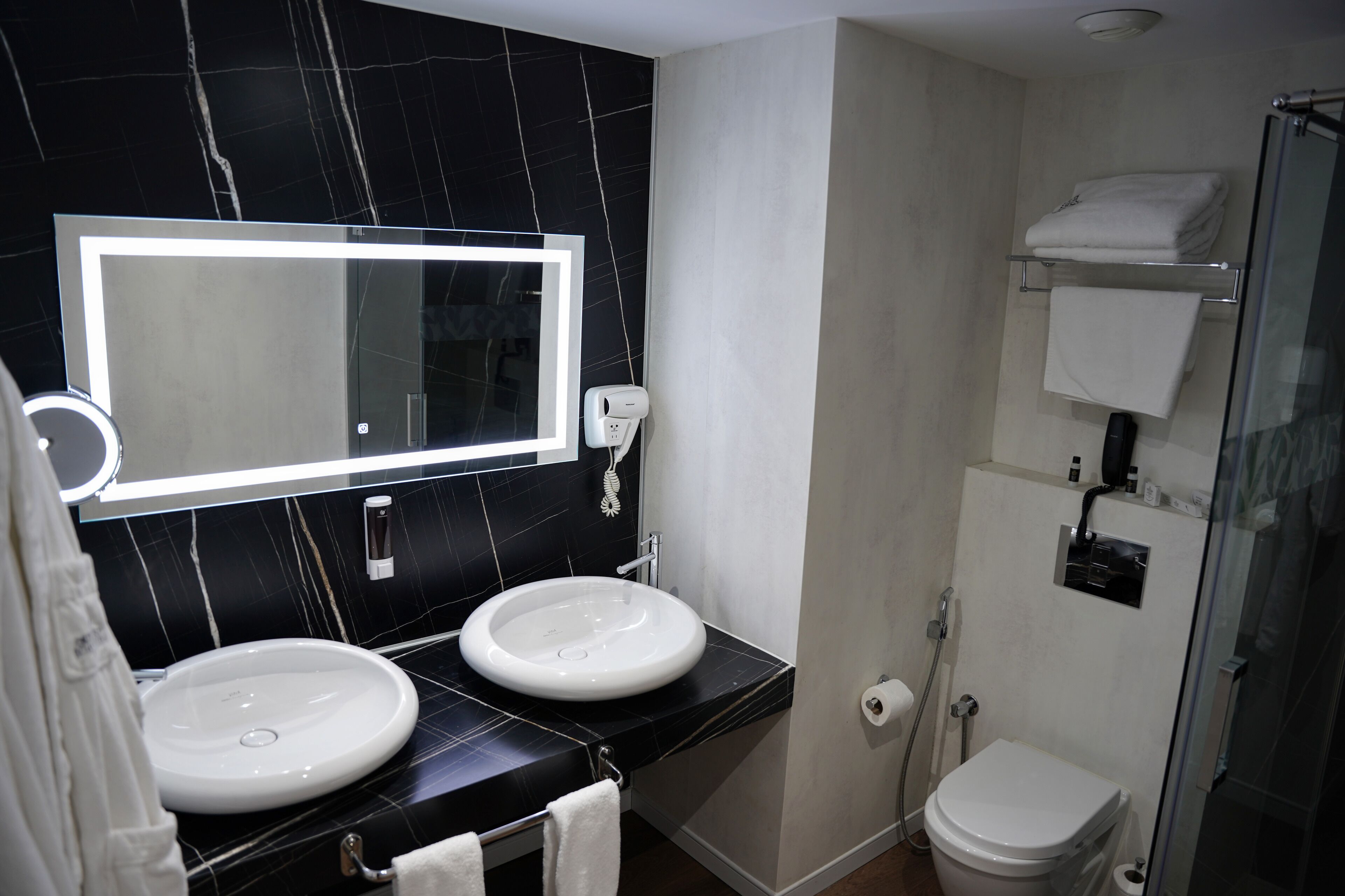 A bathroom with two sinks, a large mirror, a glass shower enclosure, and a toilet.
