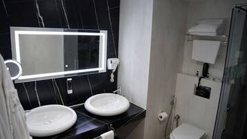 A bathroom with two sinks, a large mirror, a glass shower enclosure, and a toilet.