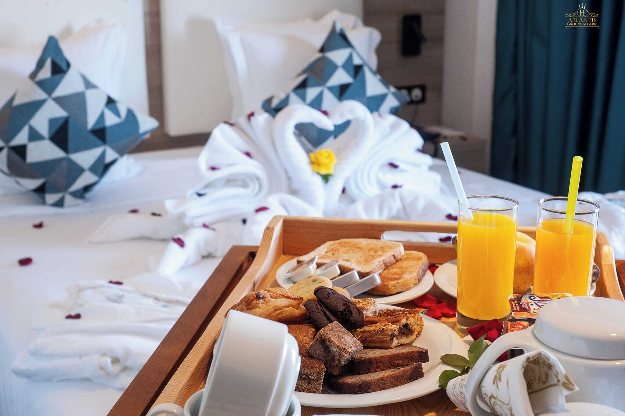 A breakfast tray with toast, pastries, and juice glasses on a hotel bed.