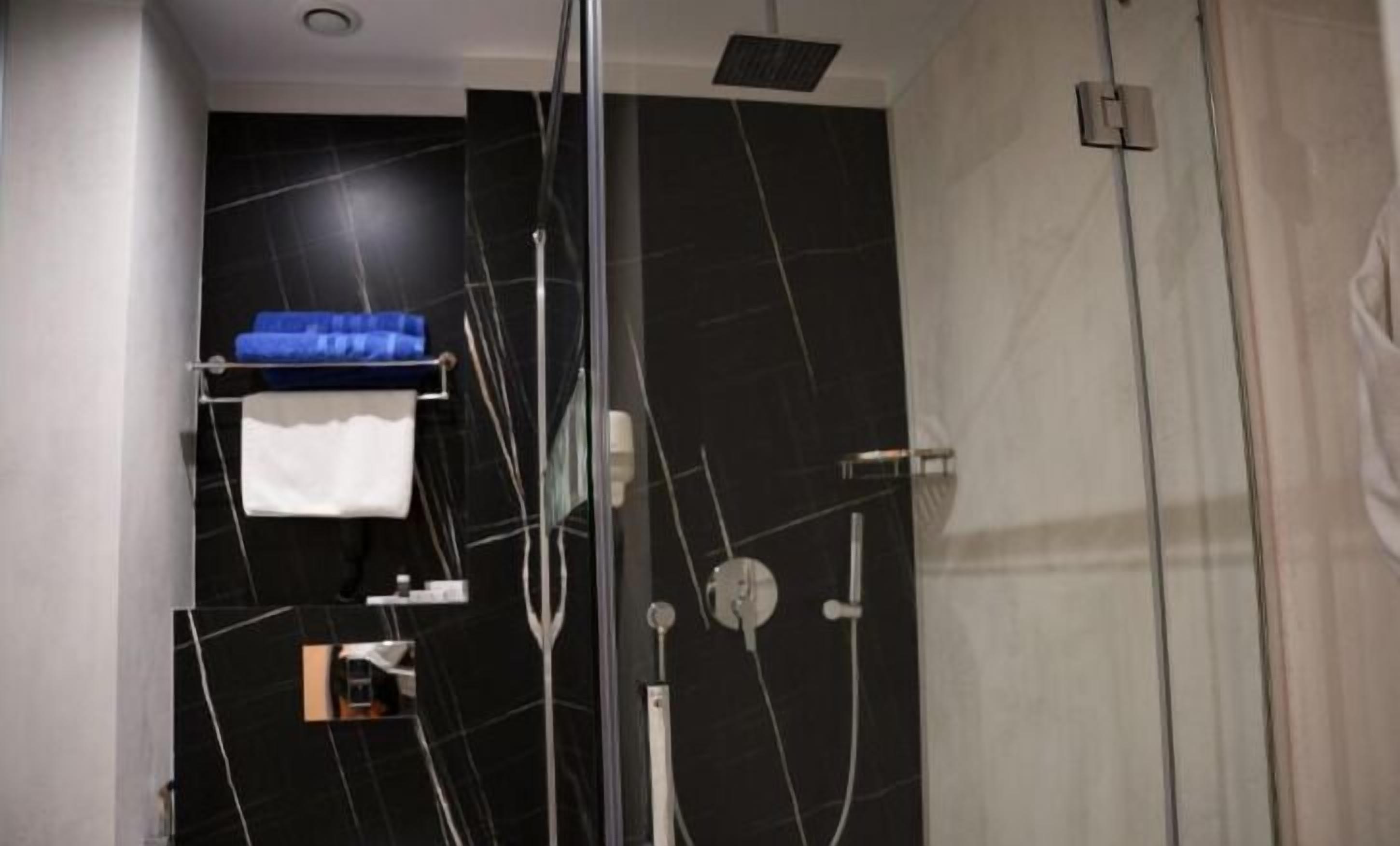 Un baño moderno con pared de mármol negro, cabina de ducha de vidrio y toallero azul.