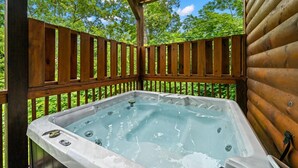 Un bain à remous installé sur une terrasse en bois à l’extérieur, avec vue sur les arbres.