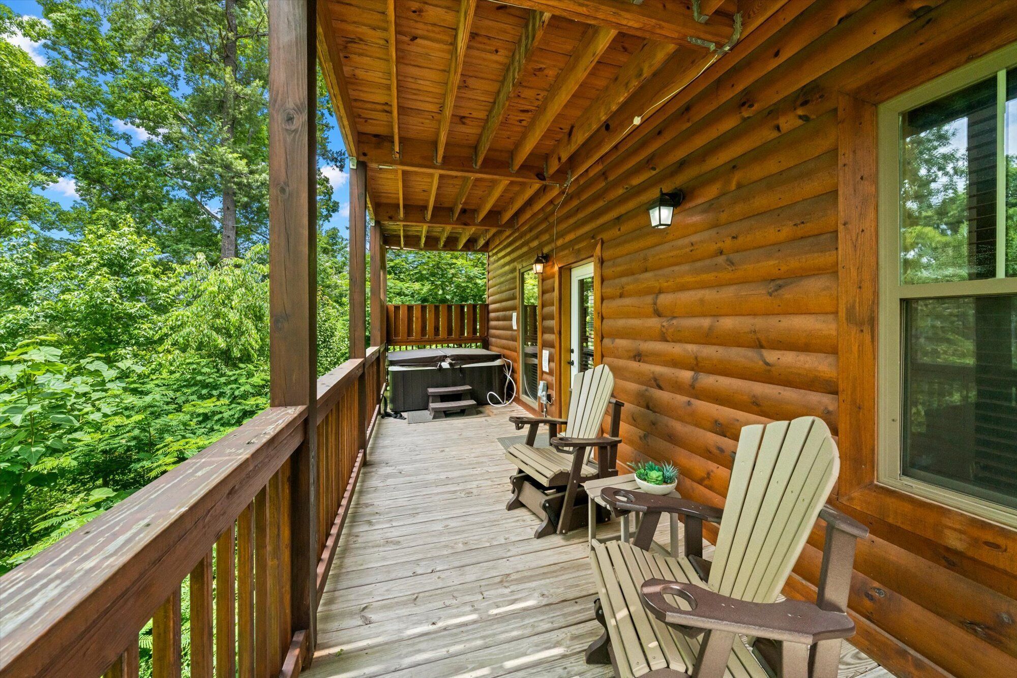 Une terrasse en bois, dotée de chaises Adirondack et d’un jacuzzi, le tout entouré d’une végétation luxuriante.