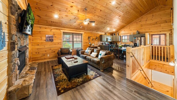 Un intérieur de chalet chaleureux avec une cheminée en pierre, des murs en bois, un coin repas et une cuisine.