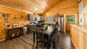 L’intérieur d’un chalet en bois comprend une cuisine, un coin repas et une fenêtre donnant sur un paysage verdoyant.