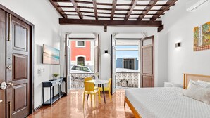 Une chambre à coucher avec un lit, une petite table et des chaises, un balcon avec vue et une porte donnant sur l’extérieur.