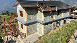 A two-story house with a stone facade, a red roof, and a green water tank on the roof. - Pari Ghar Guest House (Gilung)