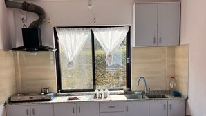 A compact kitchen with a gas stove, a sink, and a window with sheer curtains. - Pari Ghar Guest House (Gilung)