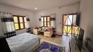 A bedroom with a bed, two chairs, a desk, and a TV. - Pari Ghar Guest House (Gilung)