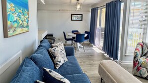 A modern living room with a blue sofa, a beige armchair, and a dining area with a table and chairs. - Beach + Golf Included Stay, Sandpiper 1003! (destin)