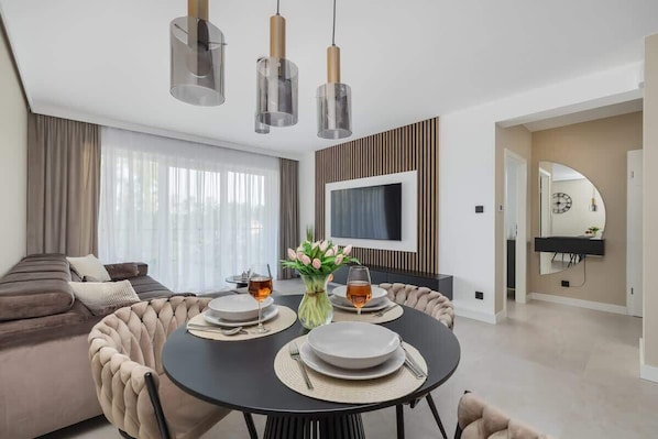 Un salon moderne avec une table à manger ronde, un canapé et un téléviseur fixé au mur.