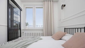 A bedroom with a bed, a window with curtains, a radiator, and a plant on the windowsill.