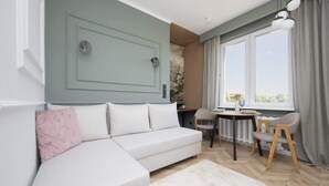 A modern living room with a white sofa, a small table, and a view of the outdoors through large windows.