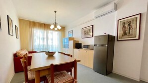 A compact kitchen with a dining table, chairs, a refrigerator, and a microwave. - Flat in a residence with pool (Porto Santa Margherita)