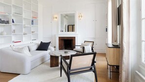 A modern living room with a white sofa, a round coffee table, and a fireplace. There are bookshelves and a TV on the wall. - A Splendide 1-BR au Quai des Orfèvres (Paris)