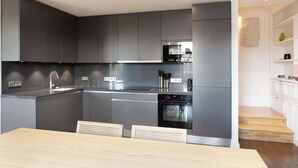 Una cocina moderna con armarios oscuros, electrodomésticos de acero inoxidable y una mesa de comedor de madera con sillas.