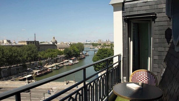 Un balcón con vista a un río, una silla y una mesa.