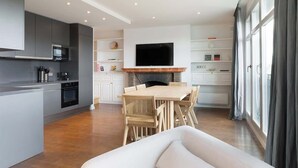 Una cocina moderna con una isla central, un comedor con mesa y sillas de madera, y un amplio ventanal con cortinas.