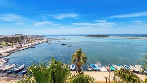 Un puerto deportivo con barcos amarrados, cielo azul despejado y vista al mar.