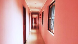 A corridor with pink walls and a tiled floor, leading to a door at the end. - Hotel Harish (Rameshwaram)