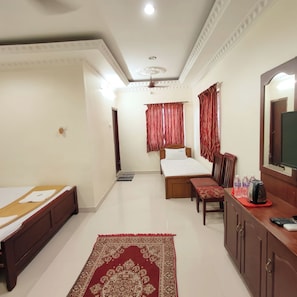 A hotel room with a bed, a desk, a chair, a TV, and a bathroom visible in the background. - Hotel Harish (Rameshwaram)