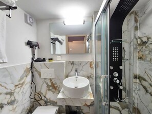 A bathroom with a marble sink, a handheld hair dryer, a glass-enclosed shower, and a mirror above the sink. - Celia Residence (Alimos)