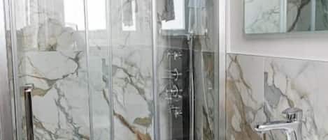 Une salle de bain moderne avec une douche à parois de verre, un lavabo blanc et des murs à motifs de marbre.