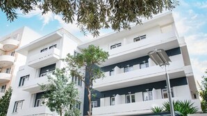 A multi-story building with balconies, a central tree, and a covered outdoor seating area. - Celia Residence (Alimos)