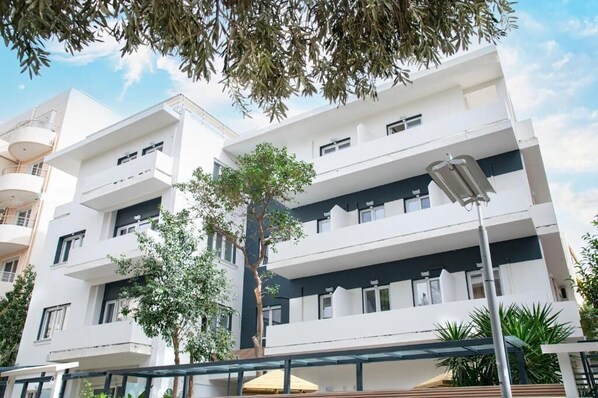 A multi-story building with balconies, a central tree, and a covered outdoor seating area. - Celia Residence (Alimos)