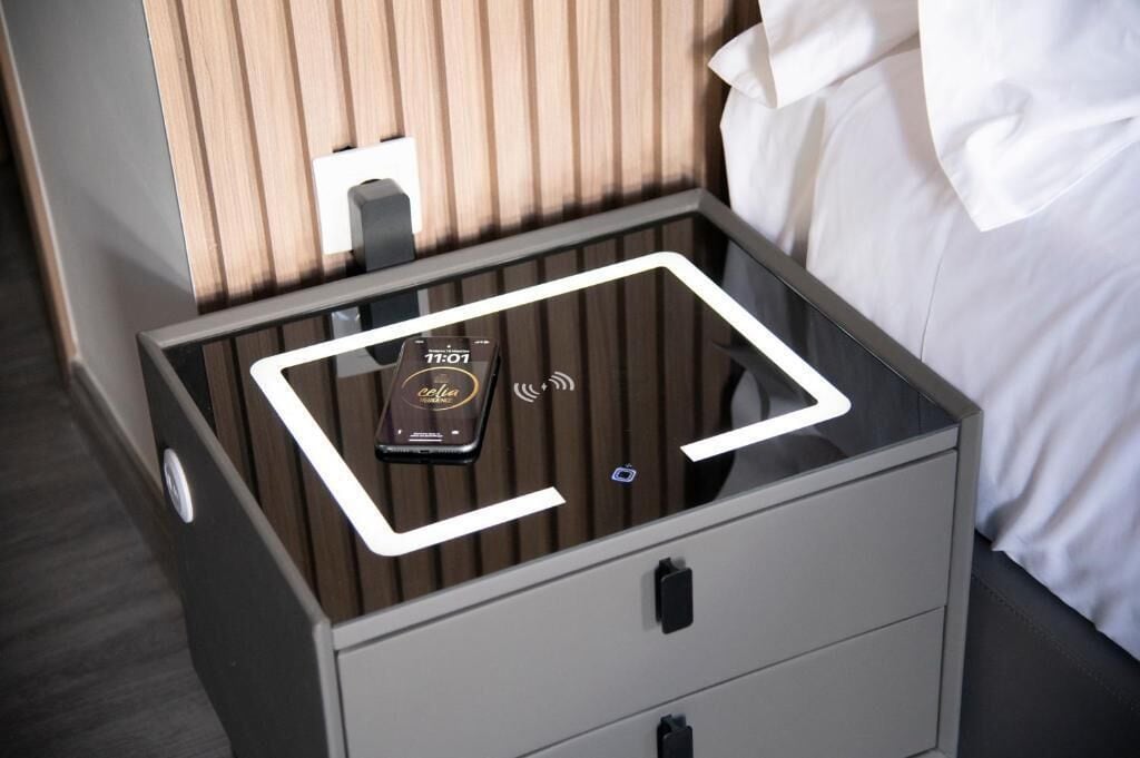 A hotel room with a glass-top bedside table, a digital clock, and a power outlet.