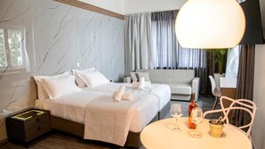 A hotel room with a bed, bedside table, and a round table with a bottle and glasses. - Celia Residence (Alimos)