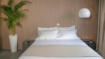 A neatly made bed with white linens, a potted plant, a bedside table, and a wall-mounted lamp.